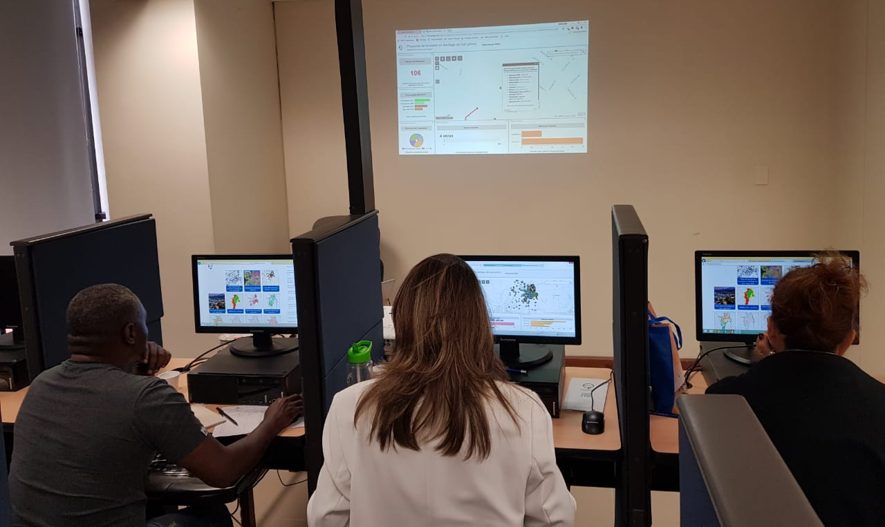 Personas ubicadas en una de las salas de capacitaciones de Comfenalco Valle, sentadas frente a computadores realizando un taller práctico de capacitación en los servicios web geográficos de la IDESC.